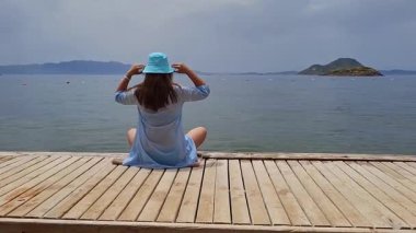 Woman enjoying serene view of ocean and distant island during sunny day at wooden dock