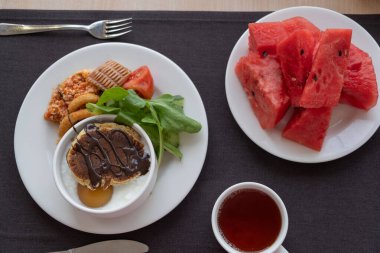 Çekici bir yemek sergisi çikolata soslu bir yığın krep, yanında da taze salata, domates ve karpuz.