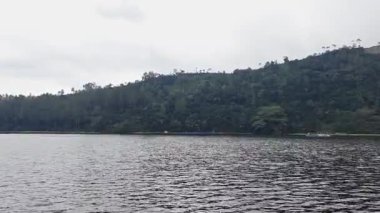 Göl bulutlu gökyüzünü ve ormanlık tepeleri yansıtır. Huzurlu bir manzara yaratır. Doğanın güzelliğini ve sükunetini gözler önüne serer..