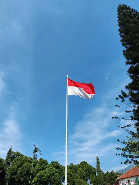Aşağıdan Endonezya bayrağı görüntüsü bir direğin üzerinde dalgalanıyor, rüzgarda dalgalanan mavi gökyüzü ve bulutlarla birlikte.