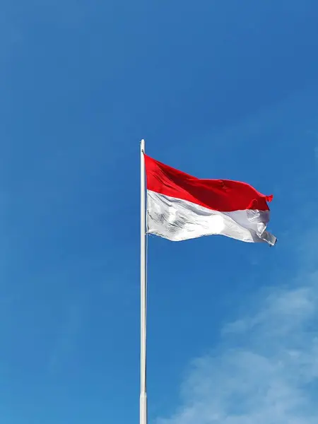 Endonezya bayrağı rüzgar tarafından dalgalanan bir direkte dalgalanıyor mavi gökyüzü ve bulutların arka planına karşı.