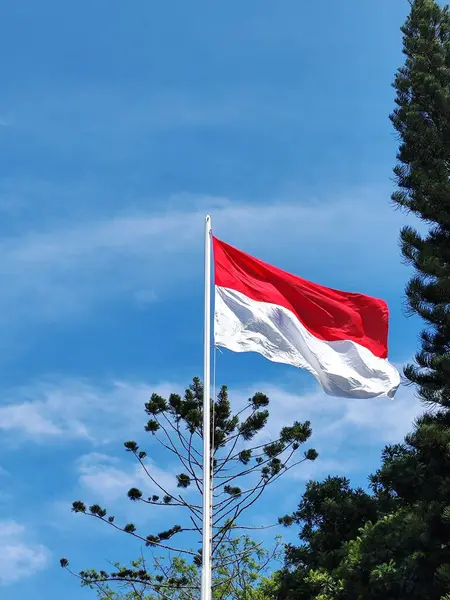 Endonezya bayrağı rüzgârla dalgalanan bir direkte mavi gökyüzü ve bulutların ardından.