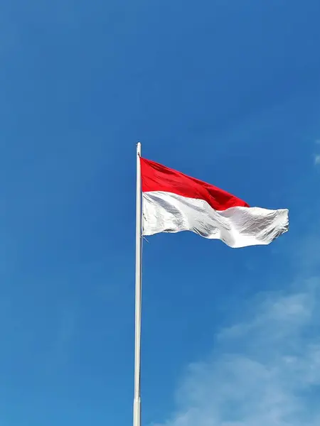 Endonezya bayrağı rüzgar tarafından dalgalanan bir direkte dalgalanıyor mavi gökyüzü ve bulutların arka planına karşı.