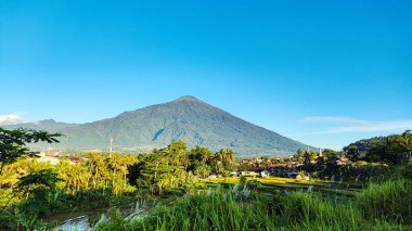 Ciremai Dağı 'nın parlak mavi arkaplanlı gölgeli ağaçlarla süslenmiş görüntüsü