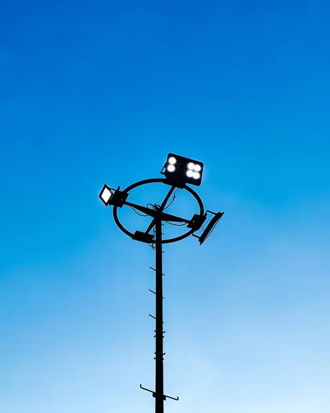 Mavi gökyüzüne karşı uzun bir projektör direğinin silueti. Şehir manzaraları, altyapı veya modern tasarımlar için ideal.