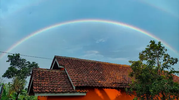 Nadir görülür, evin çatısında gökkuşağının iki katmanı var, mavi bir arka planı var.