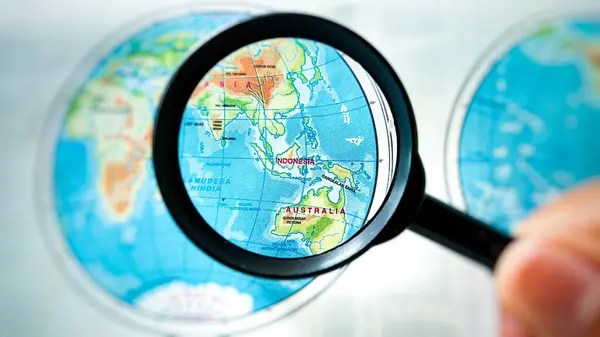 Kuningan, 19 Haziran 2025 Bir büyüteç Endonezya ve Avustralya haritasına odaklanır Bir dünya atlası içinde,.