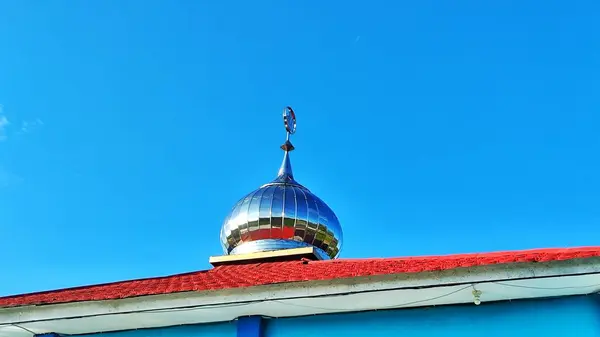 Gümüş bir kubbe ve açık mavi bir gökyüzünün altında duran kırmızı bir çatı..