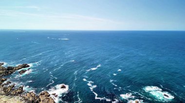 Güneşli bir günde engin bir okyanusa uzanan kayalık bir kıyı şeridi ile nefes kesici bir kıyı manzarası.