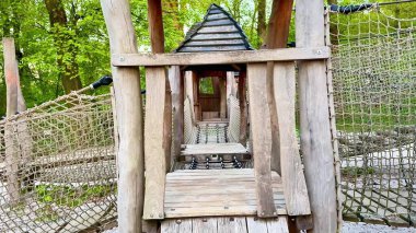 Manzaralı bir parkta büyüleyici bir ahşap oyun parkı keşfedin. Canlı bir ip köprüsü, sağlam bir merdiven, ulaşılabilir merdivenler ve hoş ahşap bir ev.