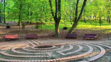 Huzurlu bir parkta, yemyeşil ağaçlar ve banklarla çevrili, rahatlama ve tefekkür için mükemmel büyüleyici tuğla bir labirent keşfedin.