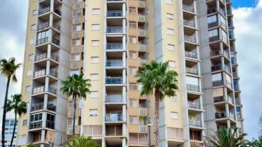 Bu video, palmiye ağaçları, balkonları ve büyük pencereleri aydınlatan, kentsel yaşam projeleri için mükemmel olan yüksek bir apartman binasını gösteriyor.