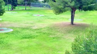 Çarpıcı ve manzaralı bir hava görüntüsü, ağaçlar ve çimlerle çevrili geniş yeşil bir golf sahası yakalıyor.