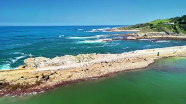 Parlak mavi okyanus ve açık gökyüzünün altındaki kayalık kıyı şeridinin nefes kesici ve çarpıcı bir görüntüsü.