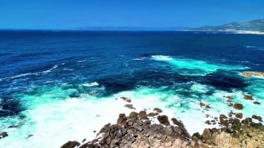 Canlı turkuaz suların çarpıcı görüntüsü sahil şeridi boyunca engebeli kayalara çarpıyor.