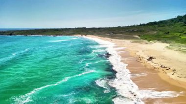 Çarpıcı bir sahil sahnesi turkuaz suları ve parlak mavi gökyüzünün altında altın kumları gösteriyor. Gerçek bir cennet.