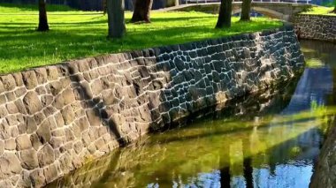 Yumuşak bir nehrin yemyeşil sulardan aktığı bir parkın güzelliğini tecrübe edin. Etrafı ağaçlar ve taş duvarlarla çevrili. Huzuru davet ediyor.