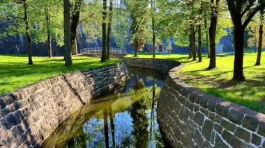 Yumuşak bir nehrin yemyeşil sulardan aktığı bir parkın güzelliğini tecrübe edin. Etrafı ağaçlar ve taş duvarlarla çevrili. Huzuru davet ediyor.