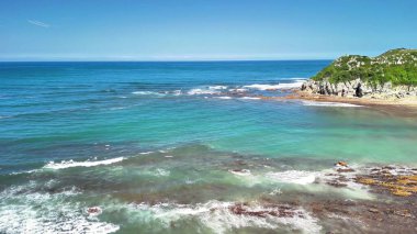 Sakin ve sakin bir sahil şeridinin nefes kesici manzarası el değmemiş turkuaz sular ve yemyeşil bitki örtüsü sergiliyor.