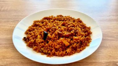 Canlı ve renkli bir tabak Jollof pilavı güzel bir şekilde zengin rengini ve bir dizi lezzetli malzemesini sergiliyor.