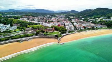 Bu hava görüntüsü, kumlu bir sahili ve çevresini çevreleyen yemyeşil manzaraları olan bir kıyı kasabasını yakalıyor.
