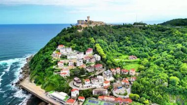 Bir hava manzarası okyanus kıyısındaki yemyeşil tepelerin arasına kurulmuş çarpıcı bir kıyı köyünü sergiliyor.