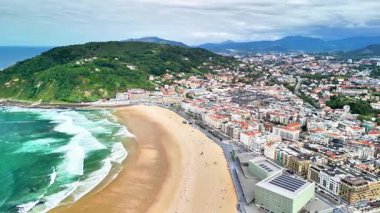 Göz kamaştırıcı hava görüntülerinde canlı bir sahil şehri sergileniyor. Resimli bir sahil ve yakınındaki yemyeşil tepeler.