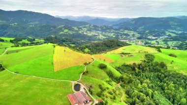 Havadan çekilen bir görüntü canlı yeşil tepeleri ve yuvarlanan manzaraları bulutlu bir gökyüzü altında yakalıyor.