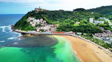 Deniz kenarına kurulmuş canlı bir sahil köyünün sersemletici hava görüntüsü, yemyeşil ve kumlu kıyıları içeriyor..