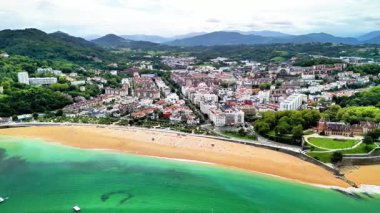 Güzel bir sahil kasabası, canlı bir şehir manzarası ve arka planda yemyeşil tepeler olan büyüleyici bir sahil manzarası.