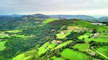 Yeşil tepeleri ve doğaya yuva yapmış büyüleyici evleri olan güzel bir manzaranın havadan görüntüsü.