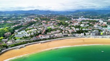 Bir hava görüntüsü güzel bir şekilde yeşil tepelerle çevrili kumlu bir sahil kasabasını yakalar.