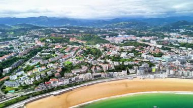 Hava manzarası, bereketli tepeler ve yumuşak bulutlu gökyüzünün altında sakin bir sahil kenti gösteriyor.