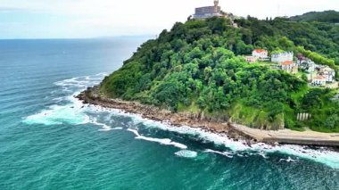 Kıyı manzarası, yemyeşil ve dramatik dalgaların kayalık kıyılara çarptığı çarpıcı bir görüntüdür.