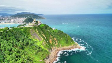 Sersemletici yeşil kayalıkların okyanus dalgalarıyla buluşması, manzaralı bir sahil şehri manzarası..