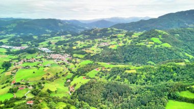 Canlı yeşil tarlaların ve dinamik, bulutlu gökyüzünün altındaki yemyeşil ormanların havadan görünüşünün tadını çıkarın.