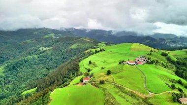 Sersemletici yeşil tepeler ve dağlarla çevrili çiftlik evleri bulutlu bir gökyüzünün altında..