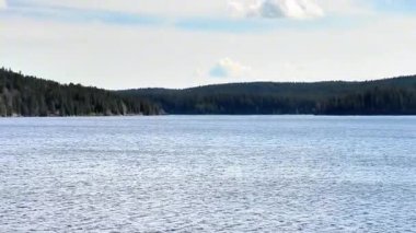 Huzurlu suların, canlı ormanların ve çarpıcı mavi gökyüzünün yer aldığı nefes kesici güzellikte bir göl manzarası.