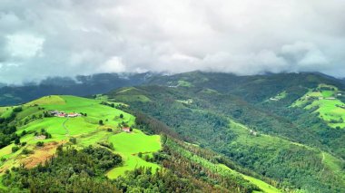 Nefes kesici bir hava manzarası bulutlu gökyüzünün altında güzel bir şekilde konumlanmış canlı yeşil tepeleri gösteriyor.