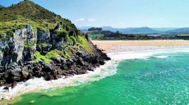 Bu hava manzarası kayalıklar ve turkuaz sularla çevrili çarpıcı bir plajı gösteriyor. Resimli bir manzara yaratıyor.