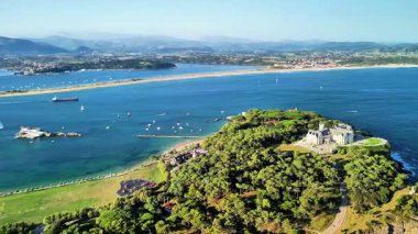 Bir hava görüntüsü, yemyeşil ve sakin mavi sularla dolu çarpıcı bir kıyı bölgesini güzelce yakalar.