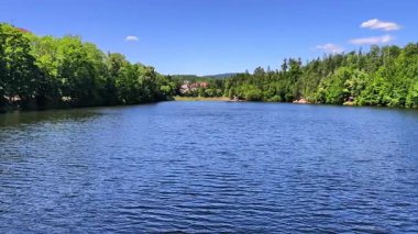Parlak ve berrak bir gökyüzünün altında canlı ağaçlar ve yansımalarının yer aldığı şaşırtıcı derecede güzel bir nehir manzarası.
