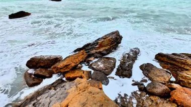 Çarpıcı kayalık sahil şeridinde taşlara çarpan turkuaz dalgalar var, doğa fotoğraflarını çekmek için mükemmel.