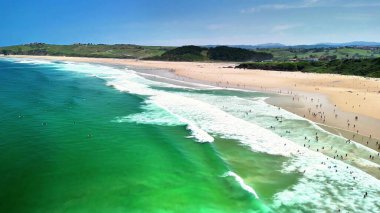 Çarpıcı hava görüntüleri, canlı bir sahil sahnesini, sörfçülerle ve berrak turkuaz sularla güzel bir şekilde gösteriyor.