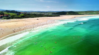 Kristal gibi berrak yeşil suları olan güzel bir sahil manzarası ve insanların eğlendiği canlı kumlu bir sahil.