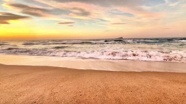 Şaşırtıcı derecede güzel bir gün batımı okyanus dalgalarını aydınlatıyor. Yakınlardaki kumlu kıyı şeridine hafifçe vuruyor.