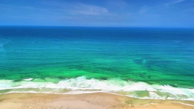 Nefes kesici bir hava manzarası canlı turkuaz okyanus dalgalarının kumlu kıyıya hafifçe vuruşunu gösteriyor.