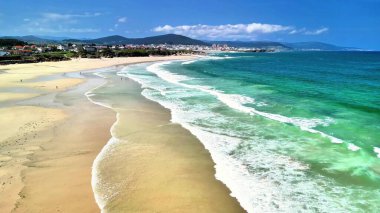 Nefes kesen bir plaj sahnesi, baş döndürücü turkuaz sular, yumuşak dalgalar ve açık mavi bir gökyüzü.