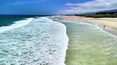 Hava manzaralı güzel, sakin, dalgalı bir sahil ve ileride güneşli bir sahil.