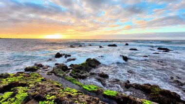 Güzel bir gün doğumu kayalık kıyı şeridini aydınlatır. Çarpıcı dalgalar ve canlı renklerle.